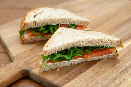 Homemade sandwich of smoked salmon, cream cheese and rocket leaves on wholemeal bread photographed on a wooden breadboard