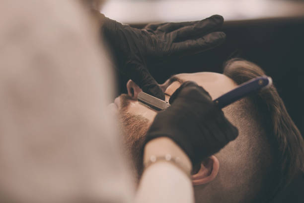 handsome, bearded man in a barbershop. Barber shaves a guy with a straight razor