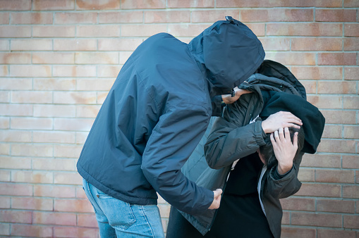 Bullying, aggression and violence scene between two males, one young adult male punches his peer near a bricks wall