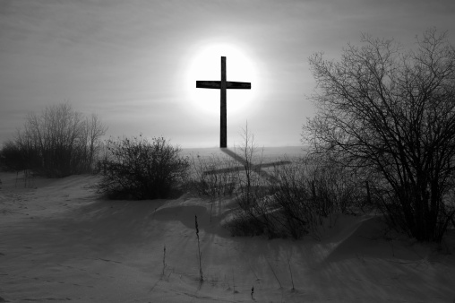 Backlit black and white cross on a snow covered field with shadow