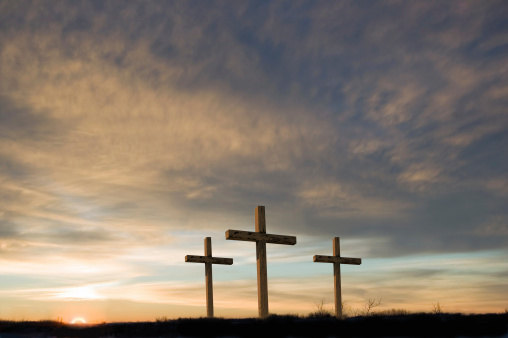 Three crosses on a hill at dawn.