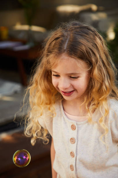 istock Cute little girl looking at a soap bubble while playing outside 1209249238