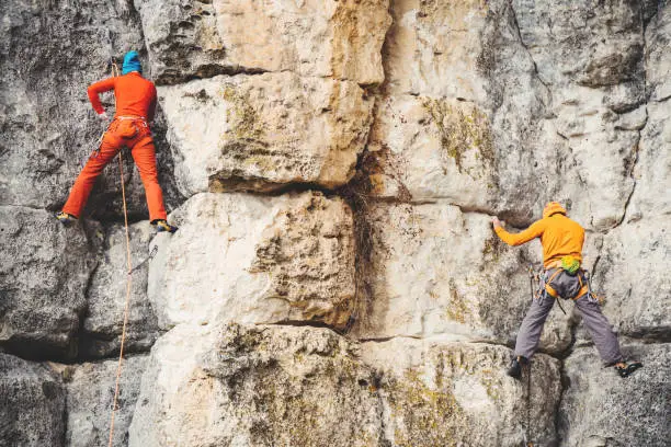 Athletic woman and man in colorful sportswear climbs a rock with rope. Sport climbing, lead. Side view. Crimea.