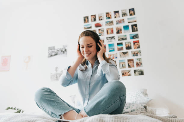 mujer joven con auriculares sentados en la cama - attractive female only young women music living room fotografías e imágenes de stock