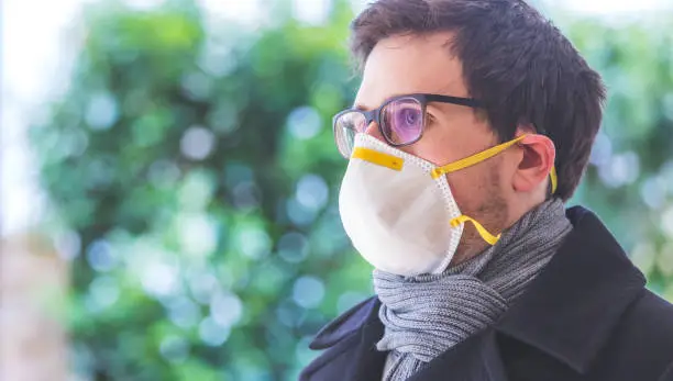 Young man outdoors with a breathing mask. Flue and corona season.