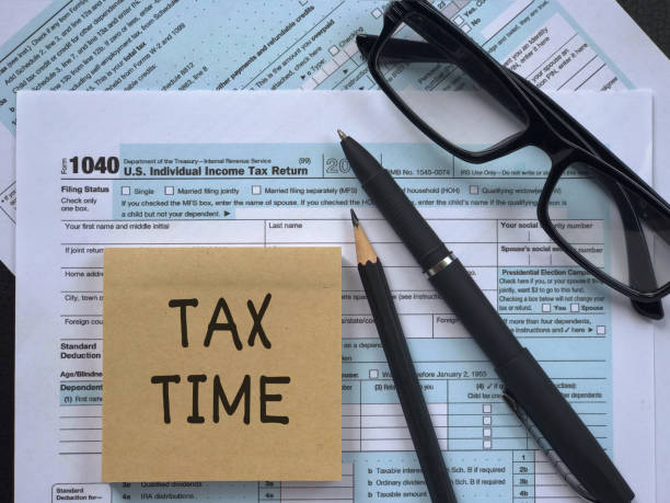 Tax-filling concept. Tax-filling concept - ‘Tax time’ written on a paper, a pencil, a pen, eyeglasses and featuring half of U.S IRS 1040 form. individual event stock pictures, royalty-free photos & images