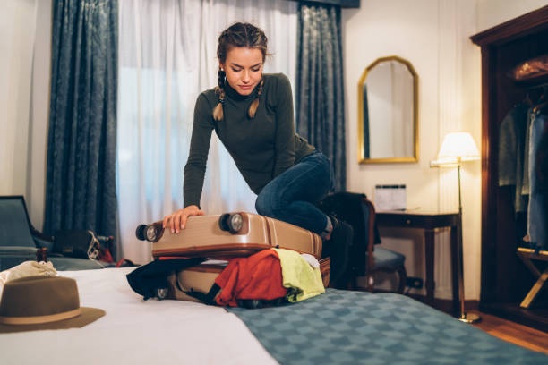 istock Woman in hotel room closing overflowing suitcase 1209258805