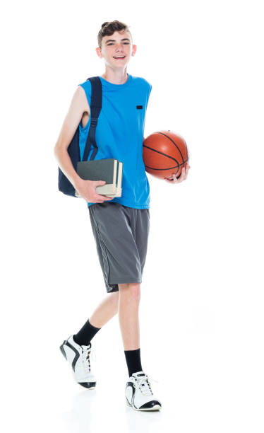 istock Caucasian young male university student walking in front of white background wearing backpack and holding textbook and using sports ball 1209263433