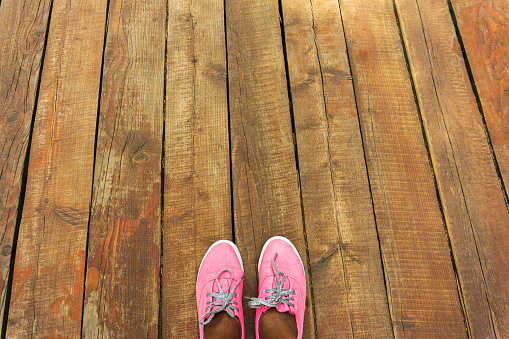 Top view of feet of a black woman in pink sneakers with silver ropes on a wooden road. People relaxation and walking by outdoor. Concept of travel lifestyle, family summer vacation.