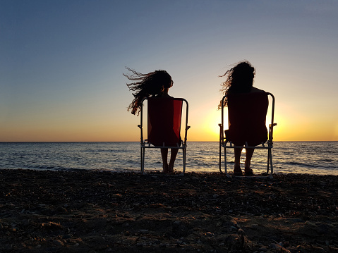 Two young girls watching the sunset at the beach