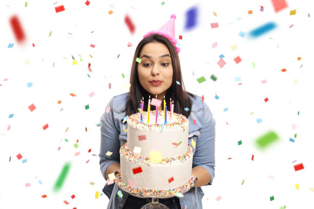 Young female celebrating birthday and blowing candles on a cake with confetti around Young female celebrating birthday and blowing candles on a cake with confetti around isolated on white background woman birthday cake stock pictures, royalty-free photos & images