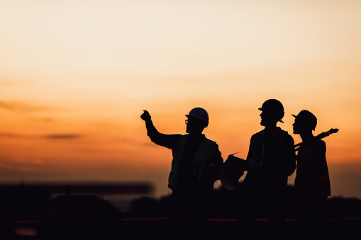 Silhouette engineer standing orders for construction crews to work on high ground heavy industry and safety concept over blurred natural background sunset pastel