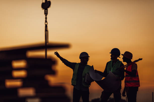 Construction workers discuss the building plans Silhouette of Survey Engineer and construction team working at site over blurred industry background with Light fair Film Grain effect construction stock pictures, royalty-free photos & images