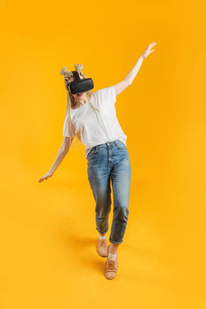 istock Young blonde woman losing balance while playing virtual reality game with headset glasses 1209267515
