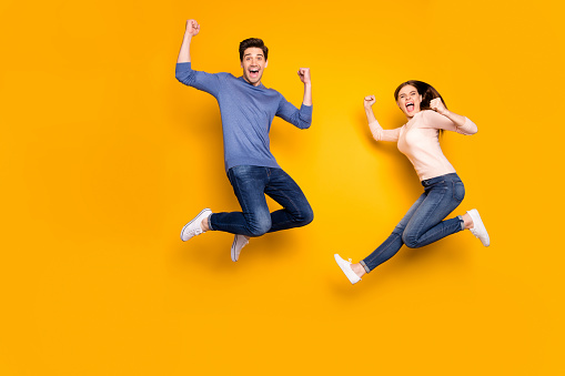Yeah we winners. Portrait of delighted two married people celebrate, lottery victory jump raise fists scream wear casual style outfit sneakers isolated over yellow color background