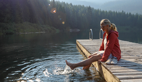 Mature woman relaxes on wooden pier, looks out across lake