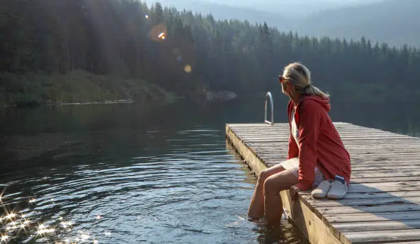 Photo of Mature woman relaxes on wooden pier, looks out across lake