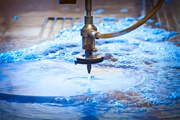 Waterjet cutting nozzle  close-up from metalwork industry. CNC waterjet machine at work cutting a steel plate.
