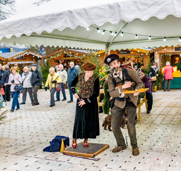 A man and woman double act entertaining visitors and shoppers at a Christmas market Bakewell, UK – November 2019. One-man band and accompanying female vocalist and spoons player entertaining the crowds. The subject of the photo was captured at an annual Christmas fayre/market held in grounds that are open to the general public. The Christmas fayre/market is free to enter, has no restrictions and available to all. chatsworth house stock pictures, royalty-free photos & images