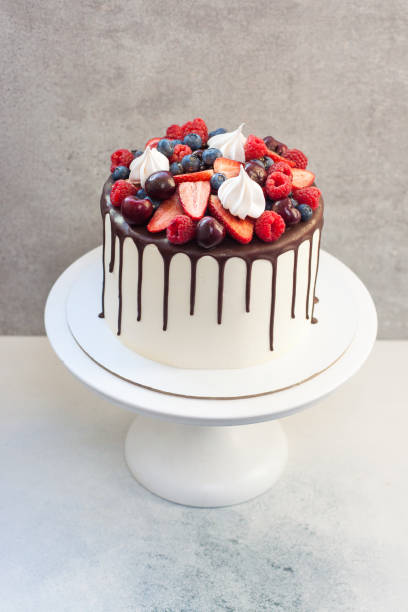istock White cake with melted chocolate, decorated with fresh strawberries, cherries, raspberries and blueberries. 1209282904