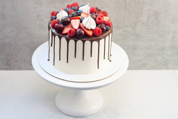 istock White cake with melted chocolate, decorated with fresh strawberries, cherries, raspberries and blueberries. 1209282914