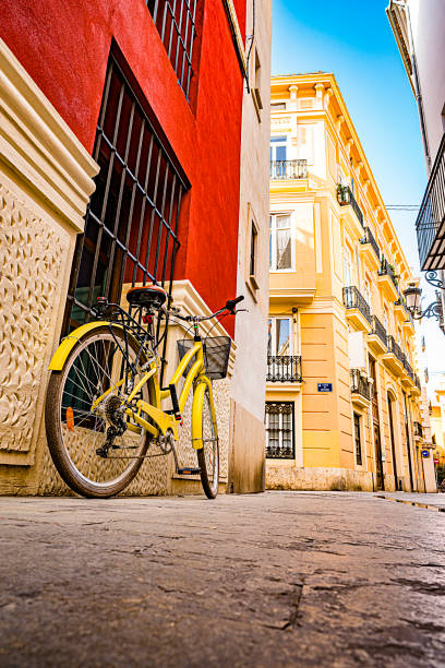 Low angle view of an old downtown street in Valencia, Spain. A yellow bicycle is on foreground. Predominant colors are yellow and red. High resolution 42Mp outdoors digital capture taken with SONY A7rII and Zeiss Batis 25mm F2.0 lens