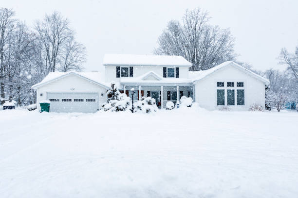 A small quaint house during a winter snowstorm. A large amount of snow has accumulated on the house and snowflakes are visible against the dark areas of the image. This would make a great home security concept image as an unshoveled house is instant notification no one is at home.