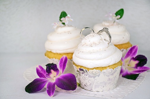 wedding rings in white frosting on cupcake with orchid blossoms