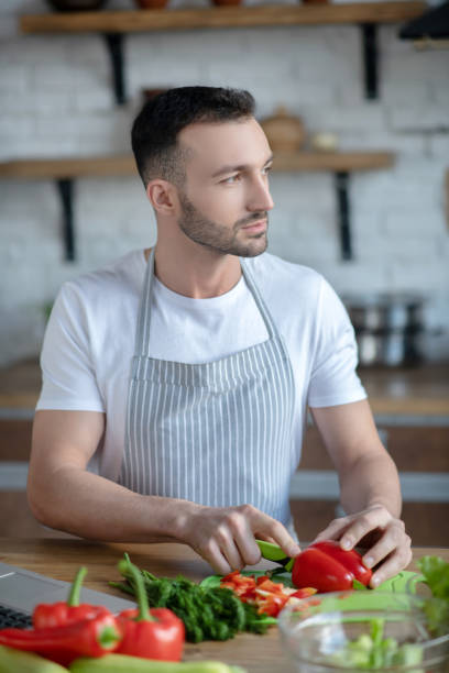 istock Good looking young man with a beard slicing pepper at home. 1209290251