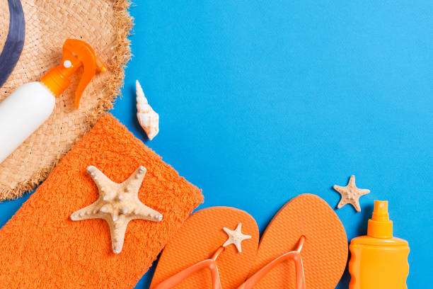 istock Summer beach flat lay accessories. Sunscreen bottle cream, straw hat, flip flops, towel and seashells on colored Background. Travel holiday concept with copy space 1209290932