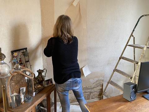 Woman is removing the old wallpaper for the new covering