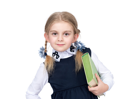 Little happy girl in school uniform holds a book, isolated on white background.