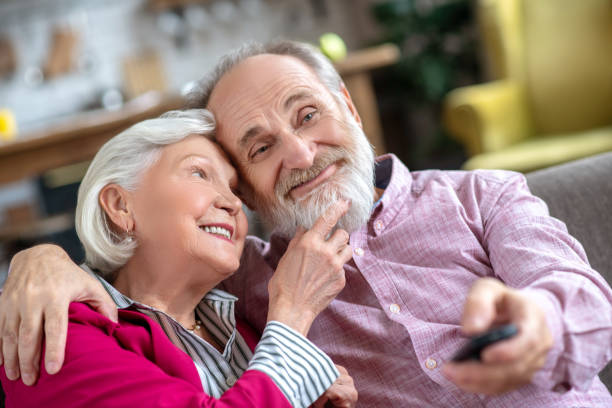 istock Grey-haired smiling woman touching her husbands beard and looking thoughtful 1209299580