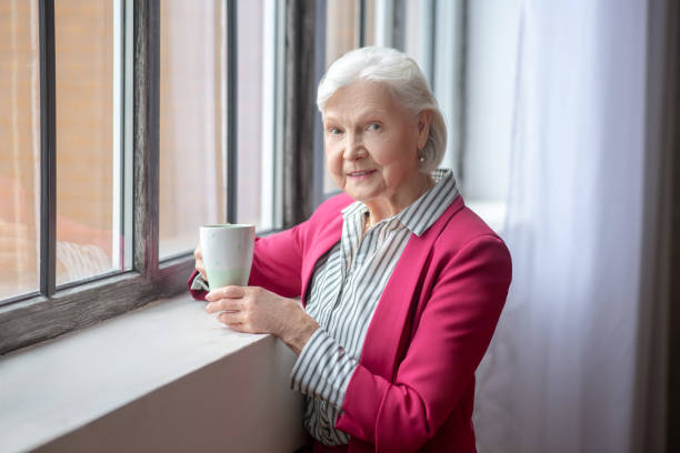 istock Grey-haired smiling lady standing at the window 1209299623
