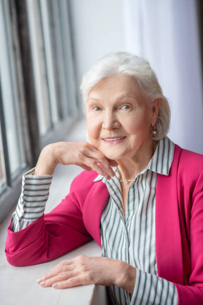 istock Grey-haired smiling lady standing near the window 1209299626