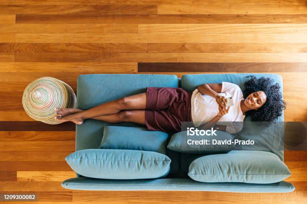 Black Woman Chatting On Smartphone Lying On Couch At Home Stock Photo - Download Image Now