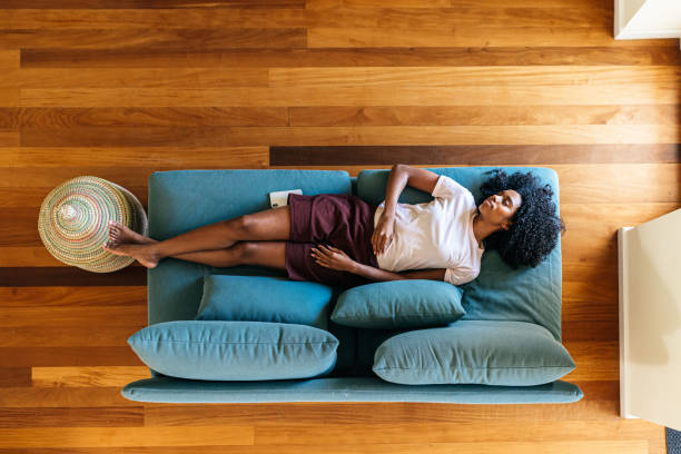 Young black lady sleeping on sofa at home Top view of African American woman in home clothing having relaxation on blue couch sleeping at home napping stock pictures, royalty-free photos & images