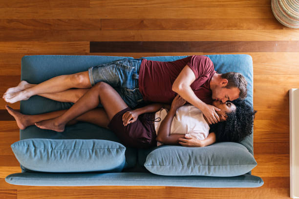 glückliche multiethnische liebhaber ruhen sich auf dem sofa aus und küssen zu hause - men sensuality photography high angle view stock-fotos und bilder
