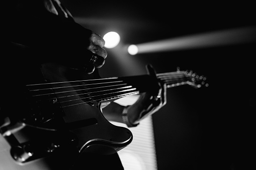 Closeup of a guitarist performing live. Hands, guitar fingerboard, and strings in deep black and white tones.
