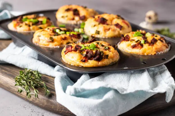 Savory muffins with bacon, quail egg, green onion and cheese on a grey stone background. Protein breakfast. Rustic style.