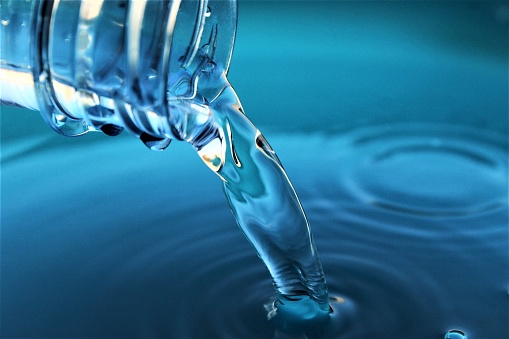 Close up poring clean water from plastic water bottle to water blue background photo isolate on blue