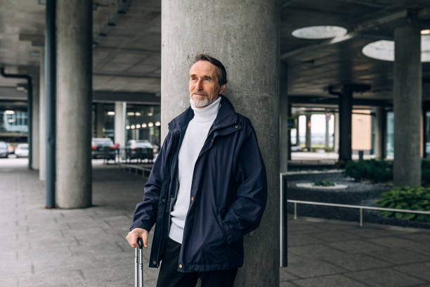 istock Stylish senior man standing outdoors at airport terminal looking away 1209307785