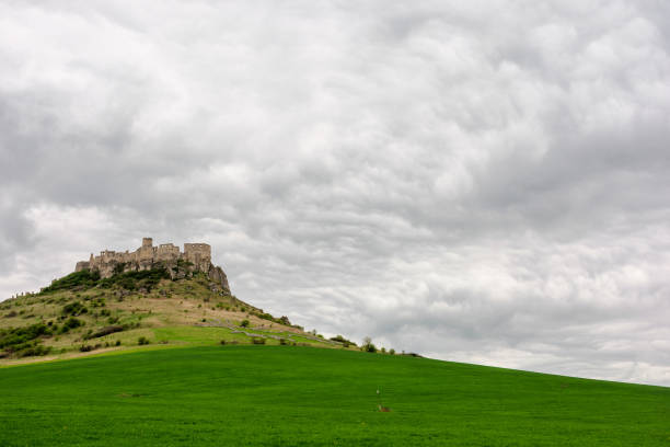 ruins of spis castle on a cloudy day in springtime. famous travel destination of slovakia. UNESCO heritage. grassy meadow at the foot of the hill.