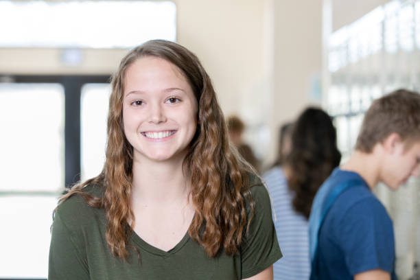 istock Cute high school girl smiles while looking at camera in high school hallway 1209311988