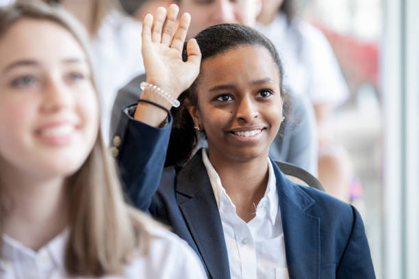 Female teenage student raises hand during lecture Female teenage student raises hand during lecture teenage high school girl raising hand during class stock pictures, royalty-free photos & images