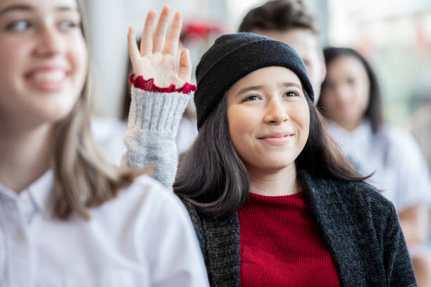 Teen girl raises her hand in classroom Teen girl raises her hand in classroom teenage high school girl raising hand during class stock pictures, royalty-free photos & images