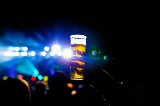 istock man holding glass of beer in a night concert. Unrecognizable crowd background. blue lights 1209317708
