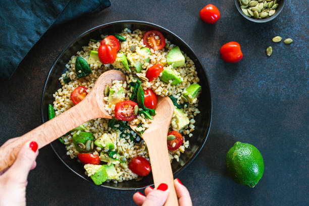 istock Hands mixing healthy salad with bulgur, avocado, spinach and cherry tomatoes. Top view. 1209318051