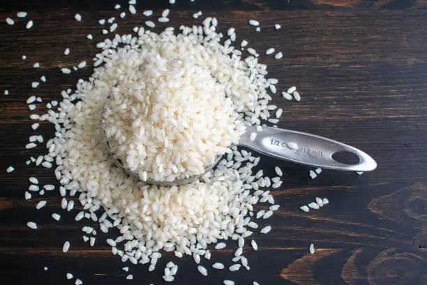 Raw short-grain rice in a measuring cup on a dark wood background