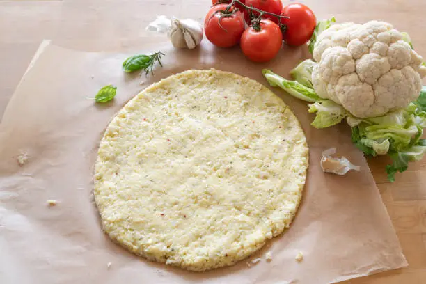Photo of raw pizza base from shredded cauliflower on baking paper, healthy vegetable alternative for low carb and ketogenic diet, copy space